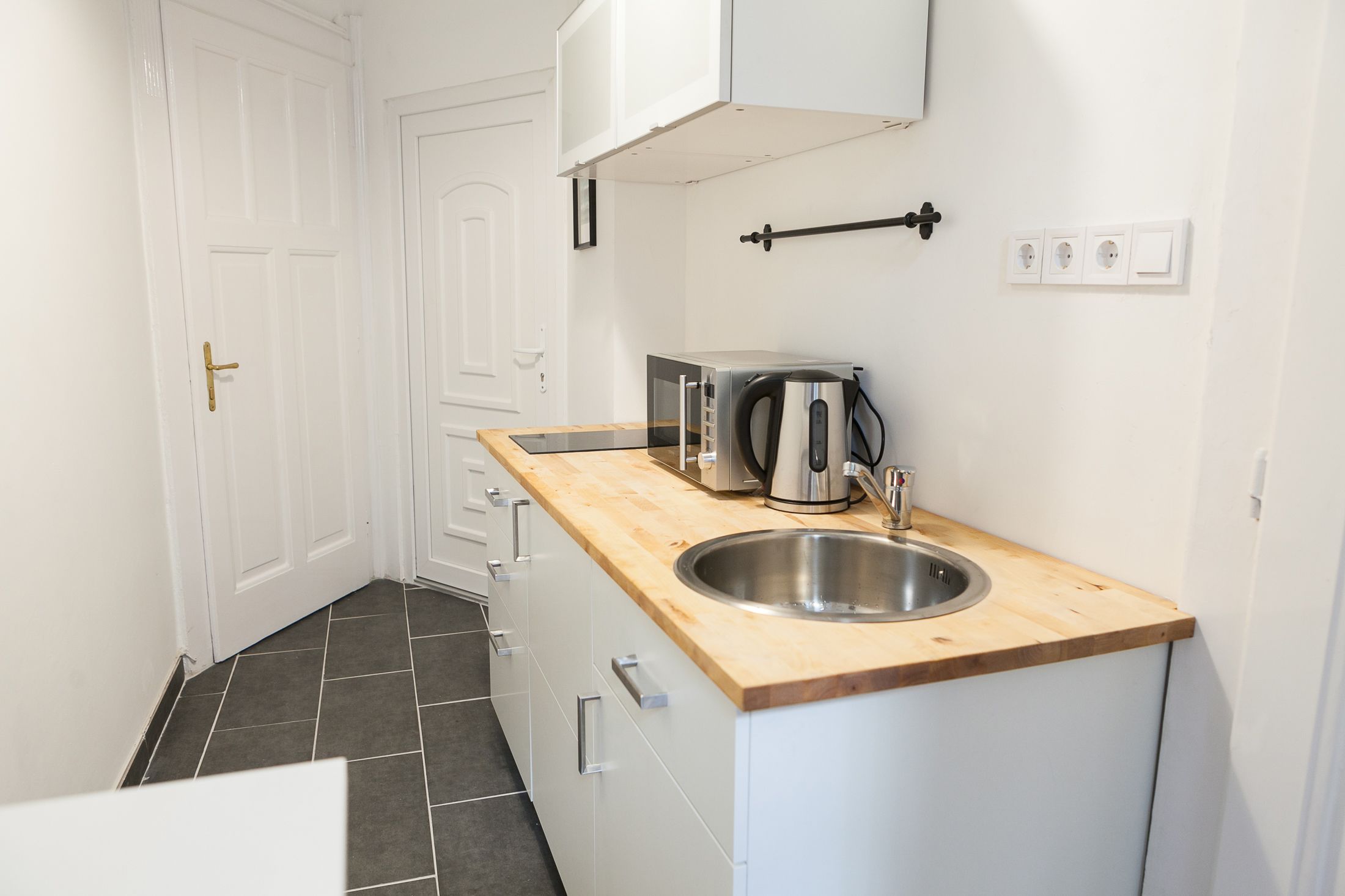 A small kitchenette with a wooden countertop, a stainless steel sink, a kettle, and a toaster.