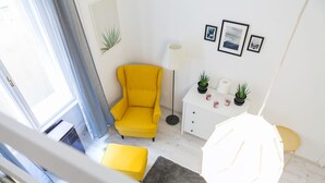 A bright living room with a yellow armchair, a white side table with plants, and a gray rug.