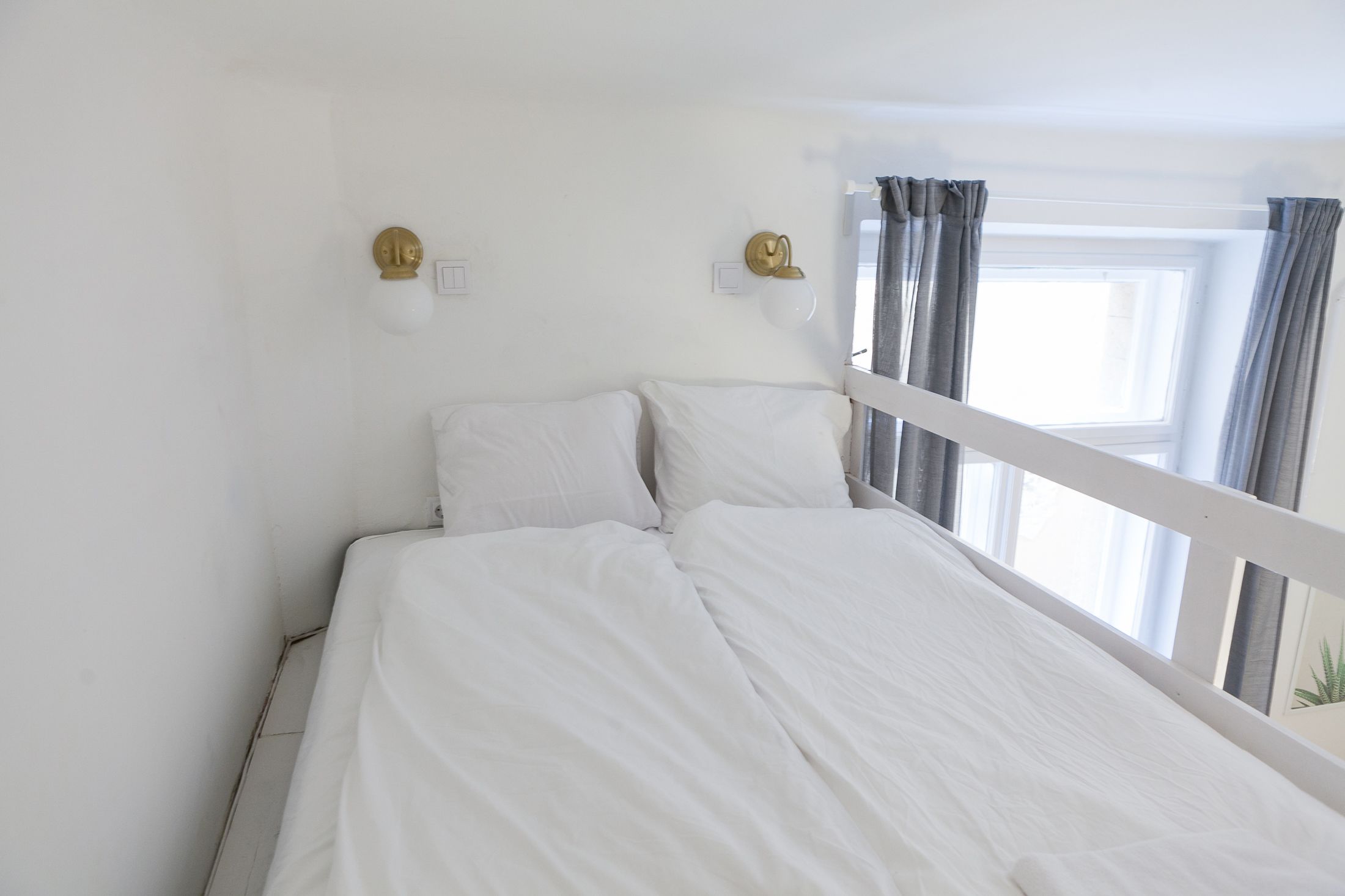 A single bed with white bedding, a white headboard, and a window with curtains.