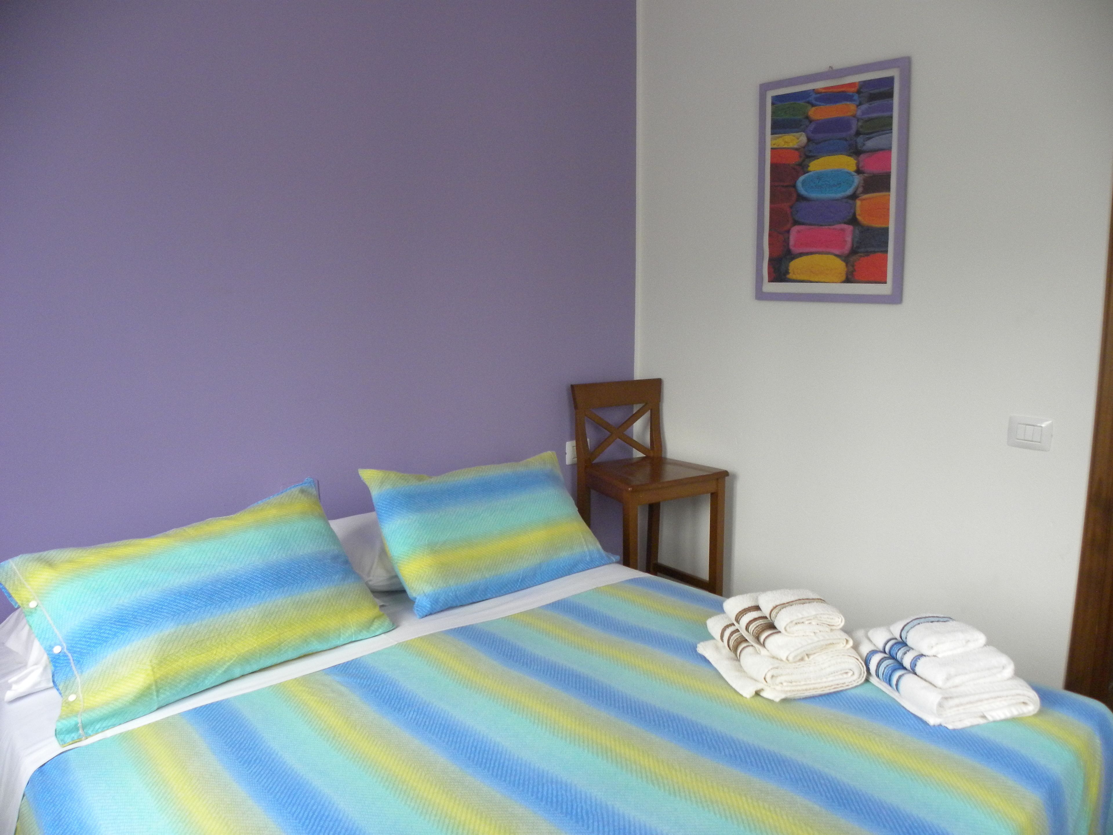 Un letto con biancheria a righe, una sedia di legno e una pila di asciugamani.