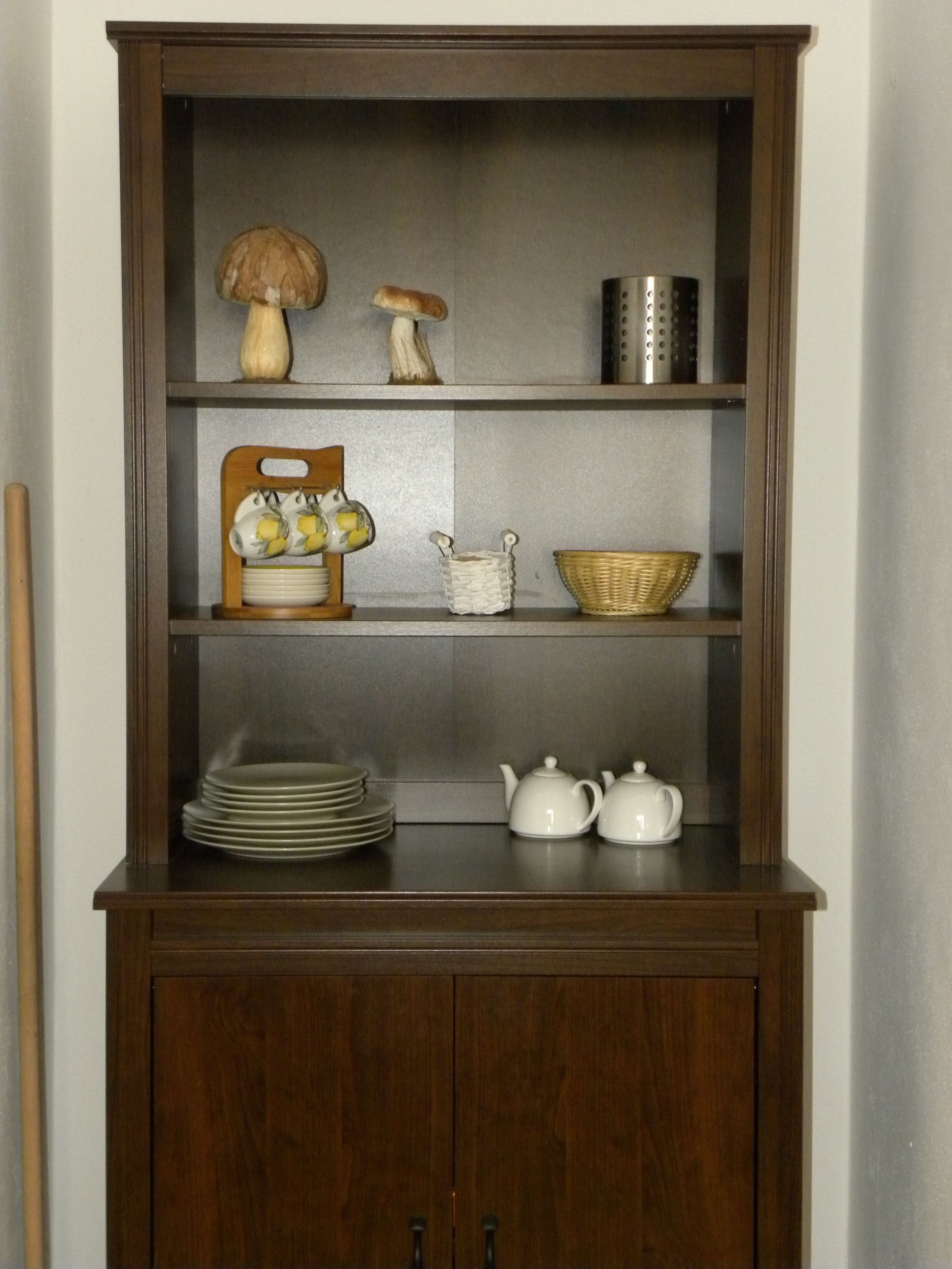 A wooden cabinet with shelves containing kitchenware, a bowl, and a decorative item.