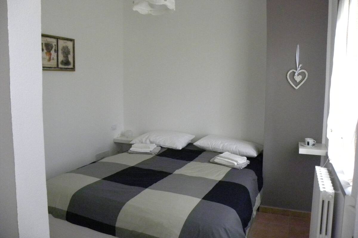 Un dormitorio con colcha a cuadros, almohadas blancas y una decoración con forma de corazón en la pared.