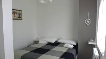A bedroom with a checkered bedspread, white pillows, and a heart-shaped decoration on the wall.