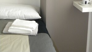 Ein ordentlich bezogenes Bett mit weißer und grauer Bettwäsche, eine herzförmige Dekoration an der Wand und ein kleiner Tisch mit Tasse und Untertasse.