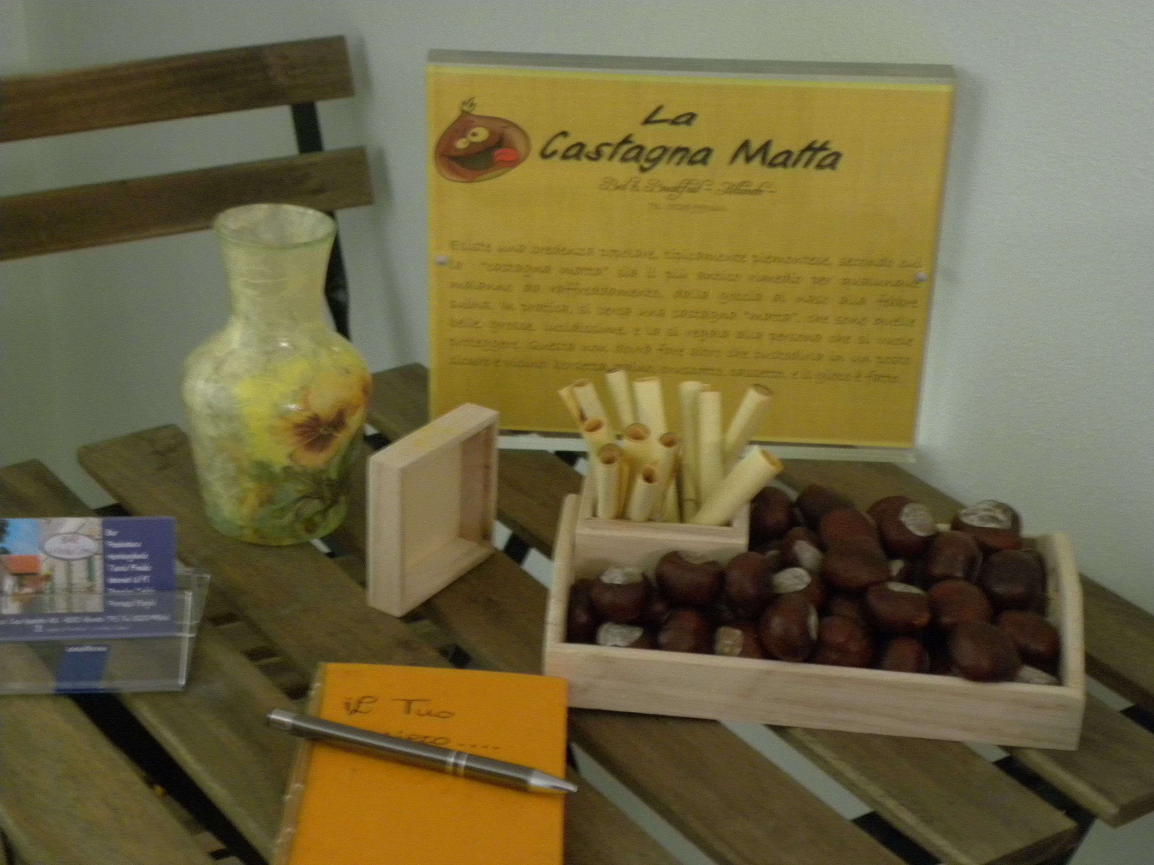 Una mesa de madera con un jarrón, una caja de avellanas, un cartel y un cuaderno.