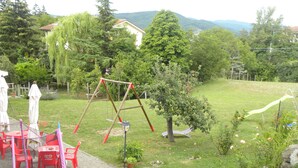 Ein Garten mit Schaukel, Trampolin und einem kleinen Gartenbereich mit Baum und Bank.