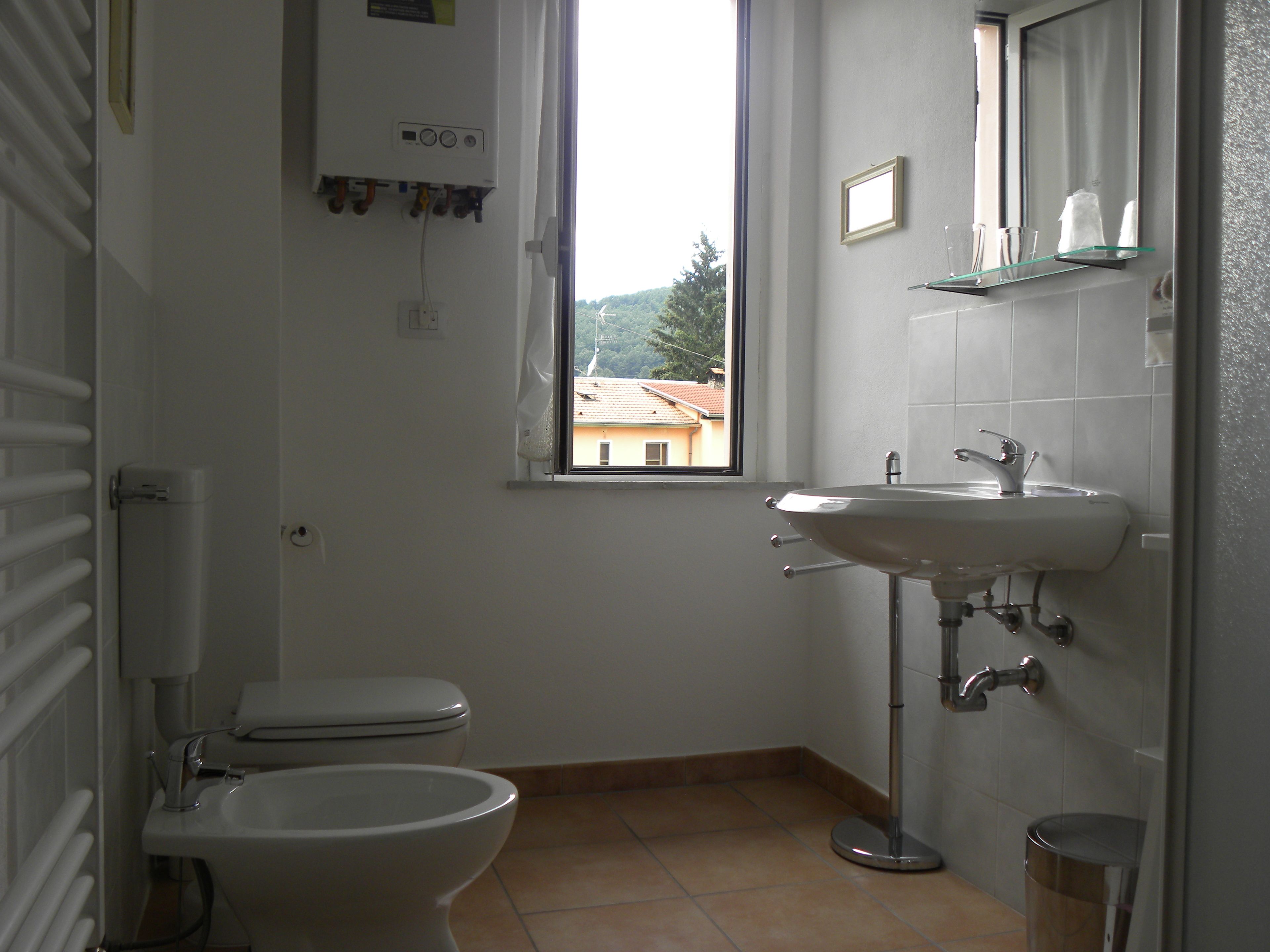 A bathroom with a toilet, bidet, sink, and a window with a view of buildings.