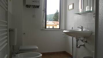 A bathroom with a toilet, bidet, sink, and a window with a view of buildings.