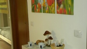Ein Hotelzimmer mit einem Bett, einer weißen Kommode mit einem Korb voller Gegenstände und einer Wand mit einem Blumenbild.
