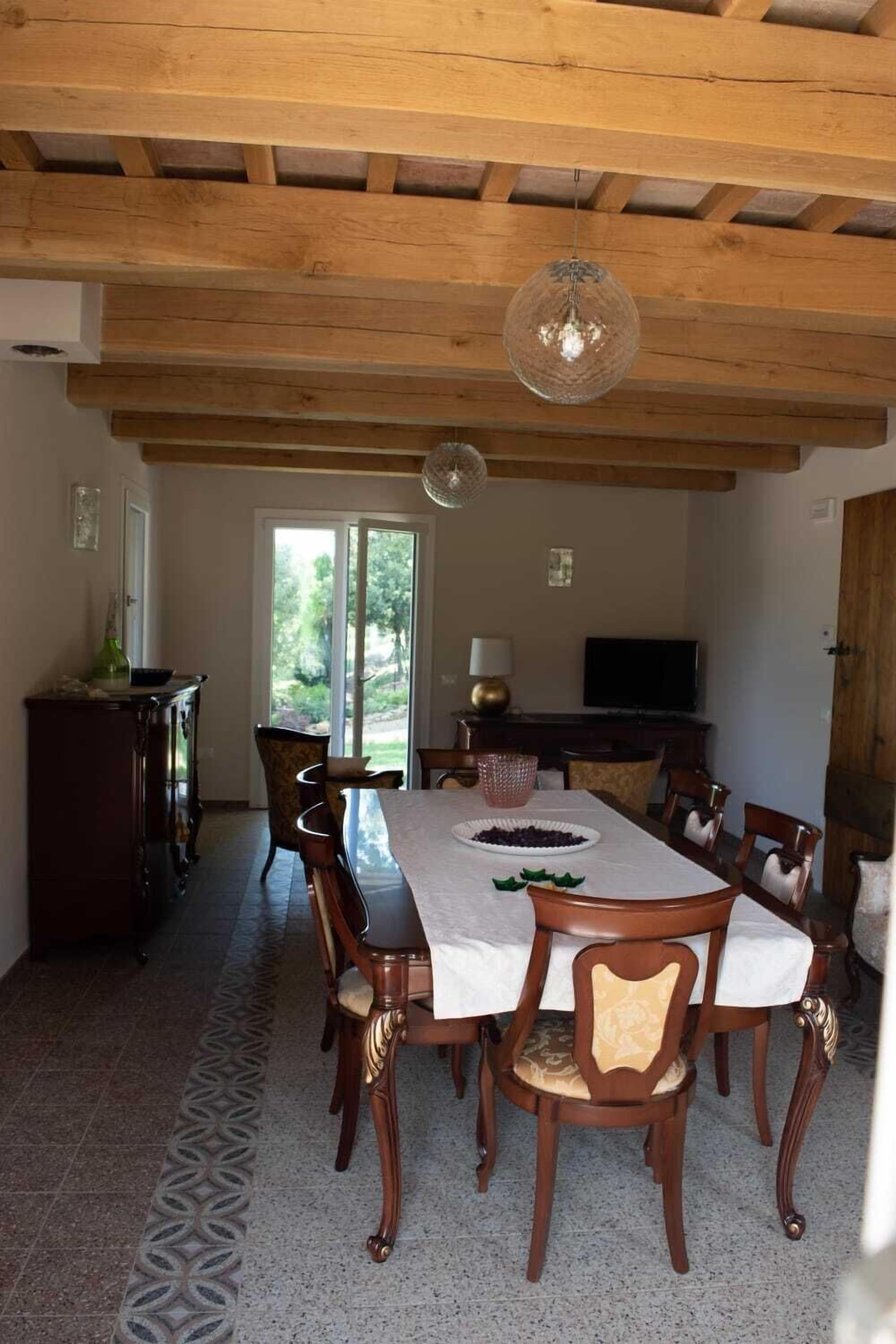 A dining area with a wooden table and chairs, a chandelier, and a television in the background.