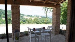 Un espacio cubierto para comer al aire libre con una mesa y sillas, con vistas a un paisaje pintoresco.