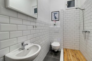 A bathroom with white tiled walls, a wooden floor, a sink, a toilet, and a shower. - Highlight Ernesto II (Budapest)