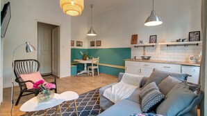 Un espacio habitable compacto con kitchenette, comedor y zona de estar con sofá y sillón.
