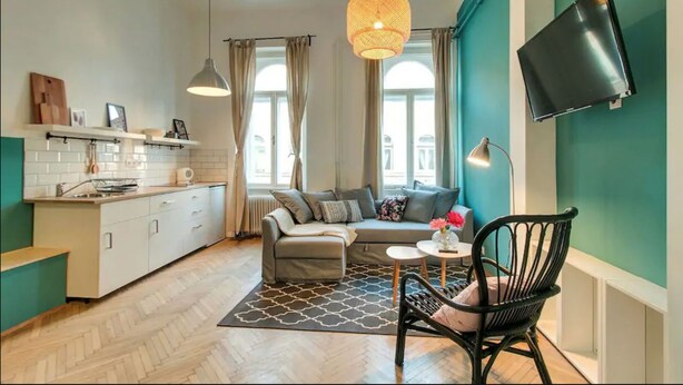 Un espacio habitable compacto con kitchenette, un sofá, una zona de comedor y un televisor montado en la pared.