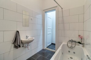 A bathroom with a white sink, a mirror, a bathtub, and a door leading to another room. - Highlight Ernesto III (Budapest)