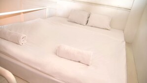 A neatly made bed with white linens and pillows, a white headboard, and a white bedside table. - Incredible Ernesto I (Budapest)