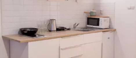 Una pequeña kitchenette con armarios blancos, un microondas, una tetera y una encimera de madera.