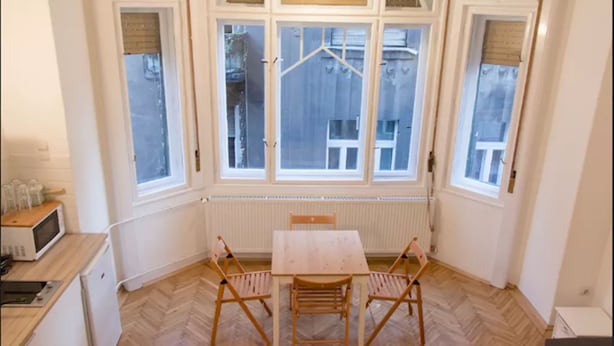 A small kitchen with a wooden herringbone floor, a white table with two chairs, and a window with a view of a building outside. - Incredible Ernesto I (Budapest)