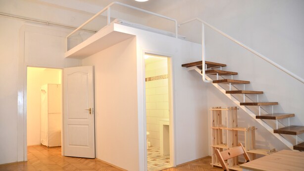 A modern interior with a wooden staircase, a dining area, and a visible bathroom. - Incredible Ernesto II (Budapest)