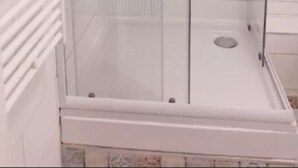 En duschkabin med glasväggar, en vit kakelbeklädd vägg och ett vitt golv.