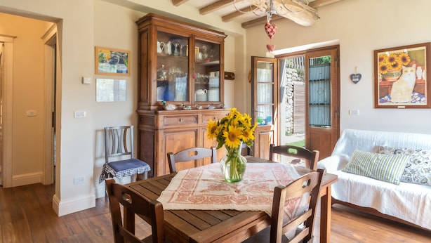 A dining area with a wooden table, chairs, a vase with sunflowers, and a wooden cabinet with glass doors. - A'Loro B&B (Terranuova Bracciolini)