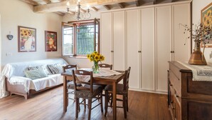 A cozy room with a wooden dining table, chairs, a sofa, and a large window with a view. - A'Loro B&B (Terranuova Bracciolini)