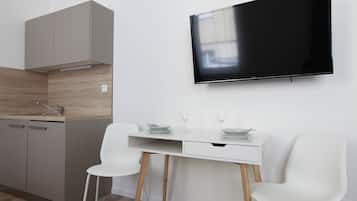 A modern kitchen with a built-in oven, a white dining table with two chairs, and a flat-screen TV mounted on the wall.