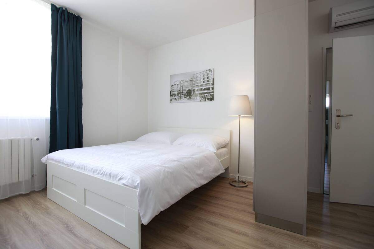 Ein Schlafzimmer mit einem weißen Bett, einer Stehlampe und einer Tür.
