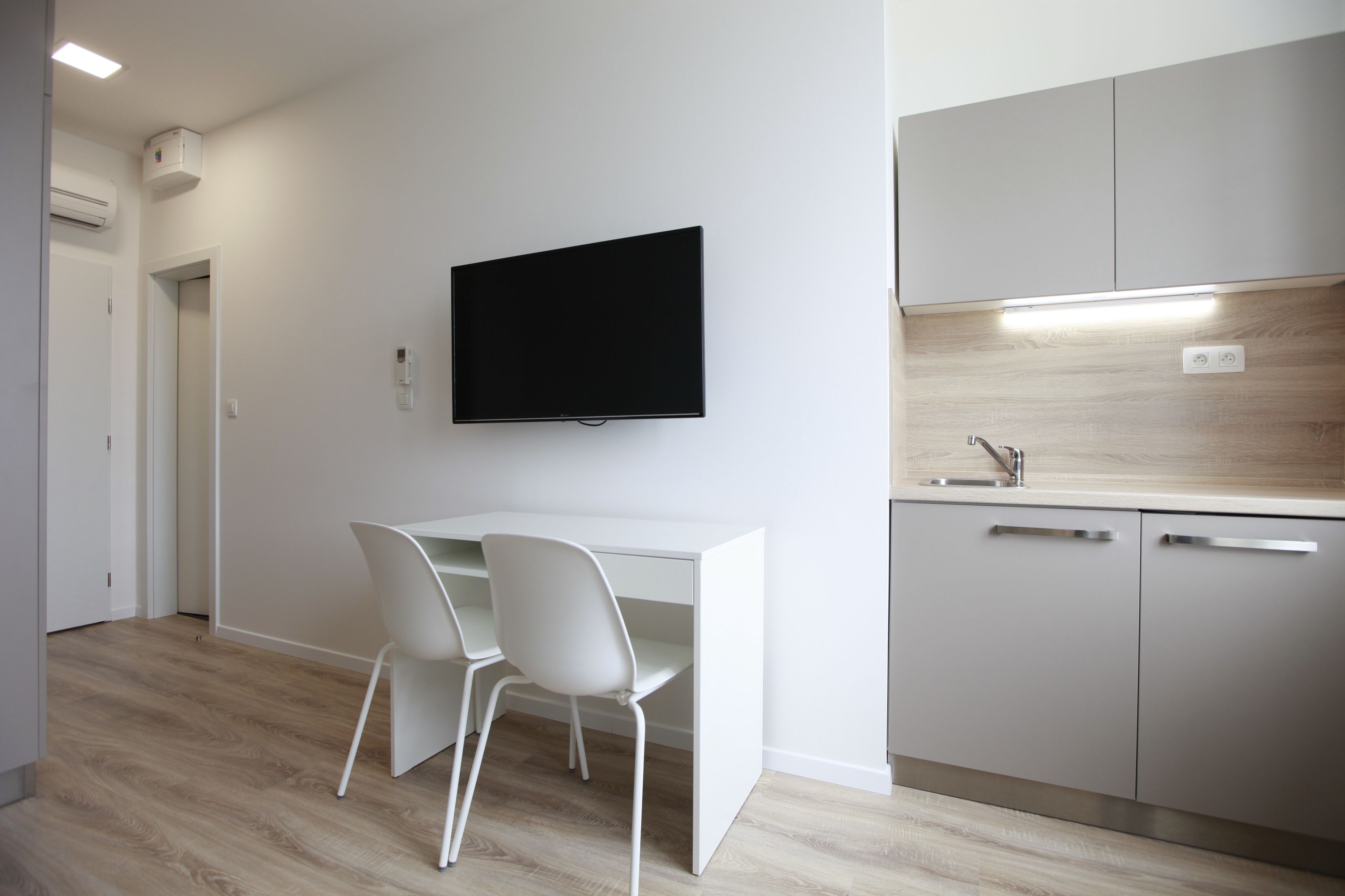 A modern kitchen with a flat-screen TV, white cabinetry, and a wooden floor.