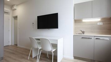 Una cocina moderna con televisor de pantalla plana, armarios blancos y suelo de madera.