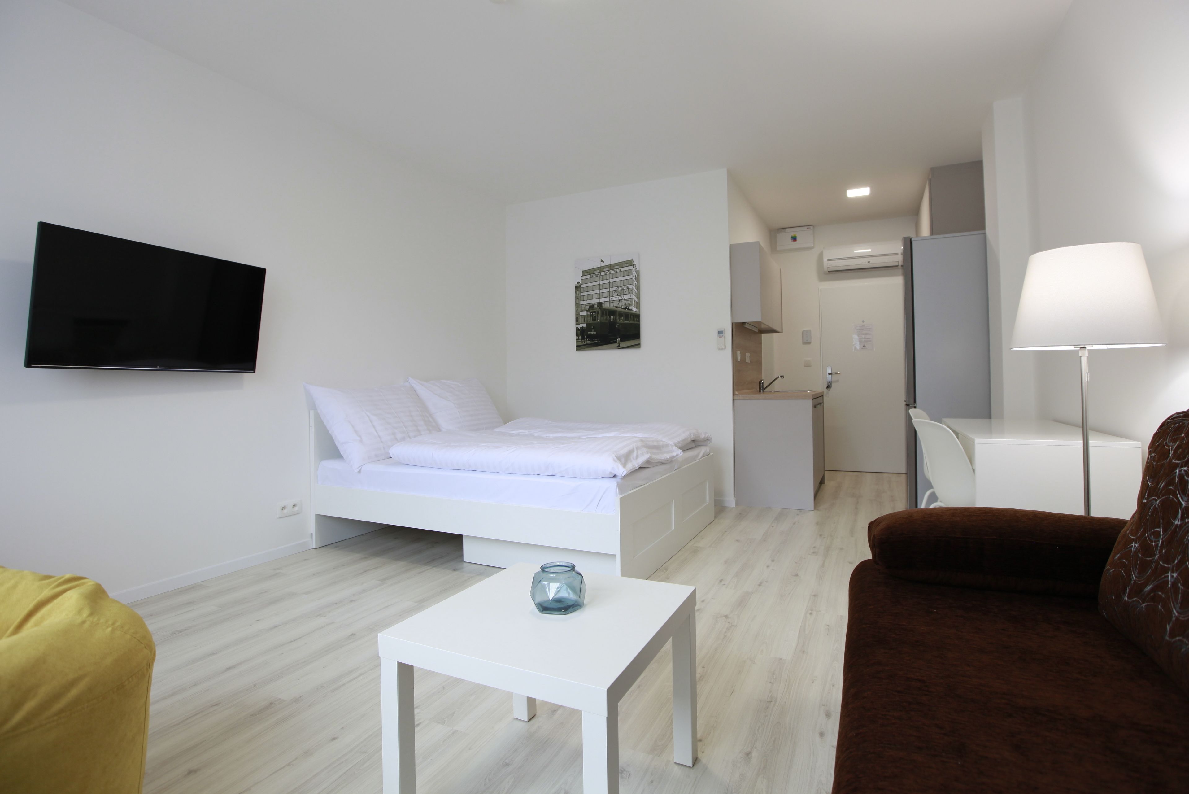 Een moderne hotelkamer met een bed, een aan de muur bevestigde televisie, een klein tafeltje en een bank.