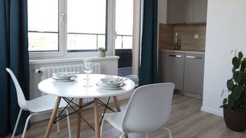 Un espace repas moderne avec une table ronde, des chaises blanches et une vue sur la cuisine et l’extérieur.
