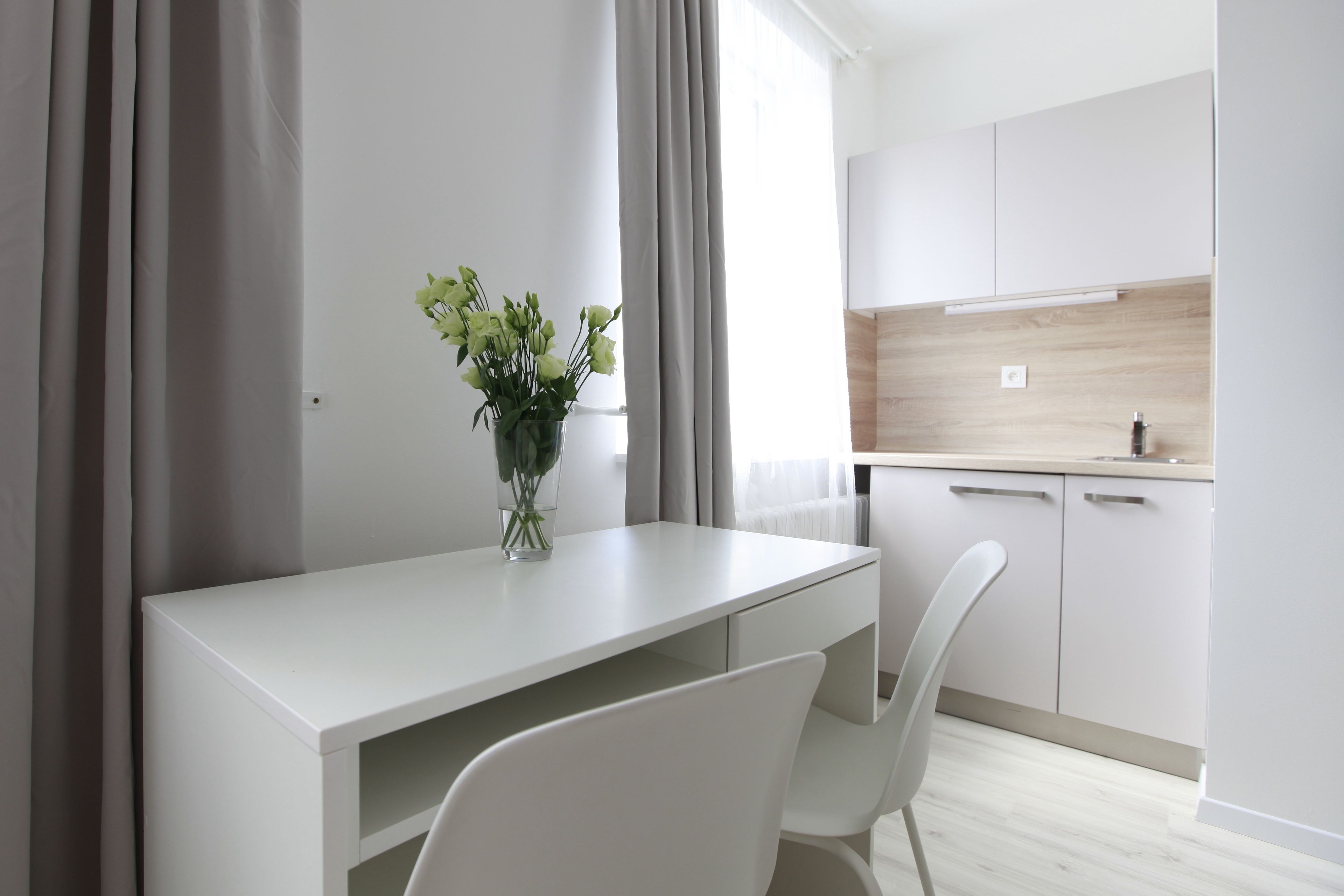 A modern kitchen with white cabinets, a white countertop, and a window with curtains.