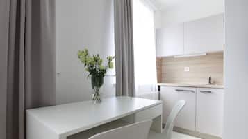 A modern kitchen with white cabinets, a white countertop, and a window with curtains.