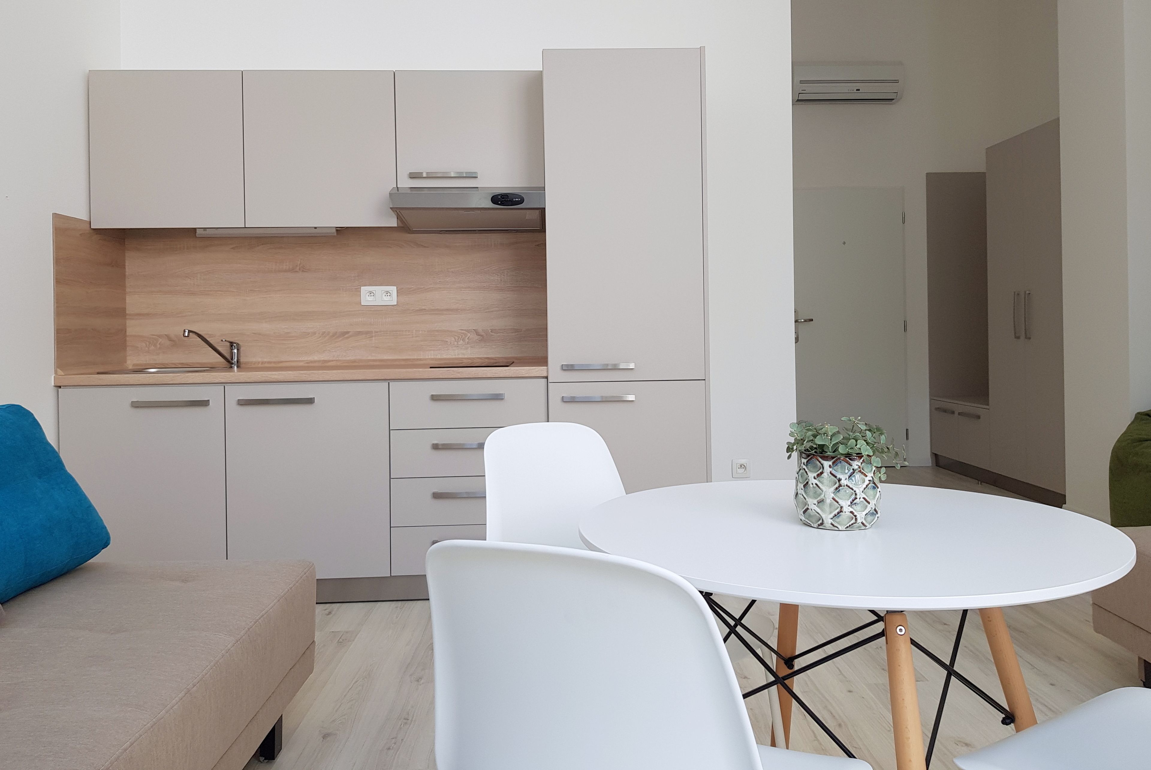 A modern kitchen with white cabinets, a wooden countertop, and a built-in stove. There is a white dining table with chairs and a potted plant.