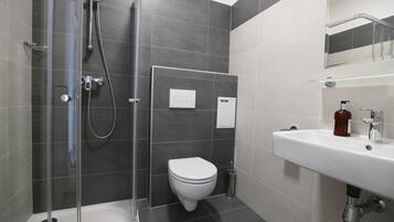 A modern bathroom with a glass-enclosed shower, a white toilet, and a sink with a soap dispenser.