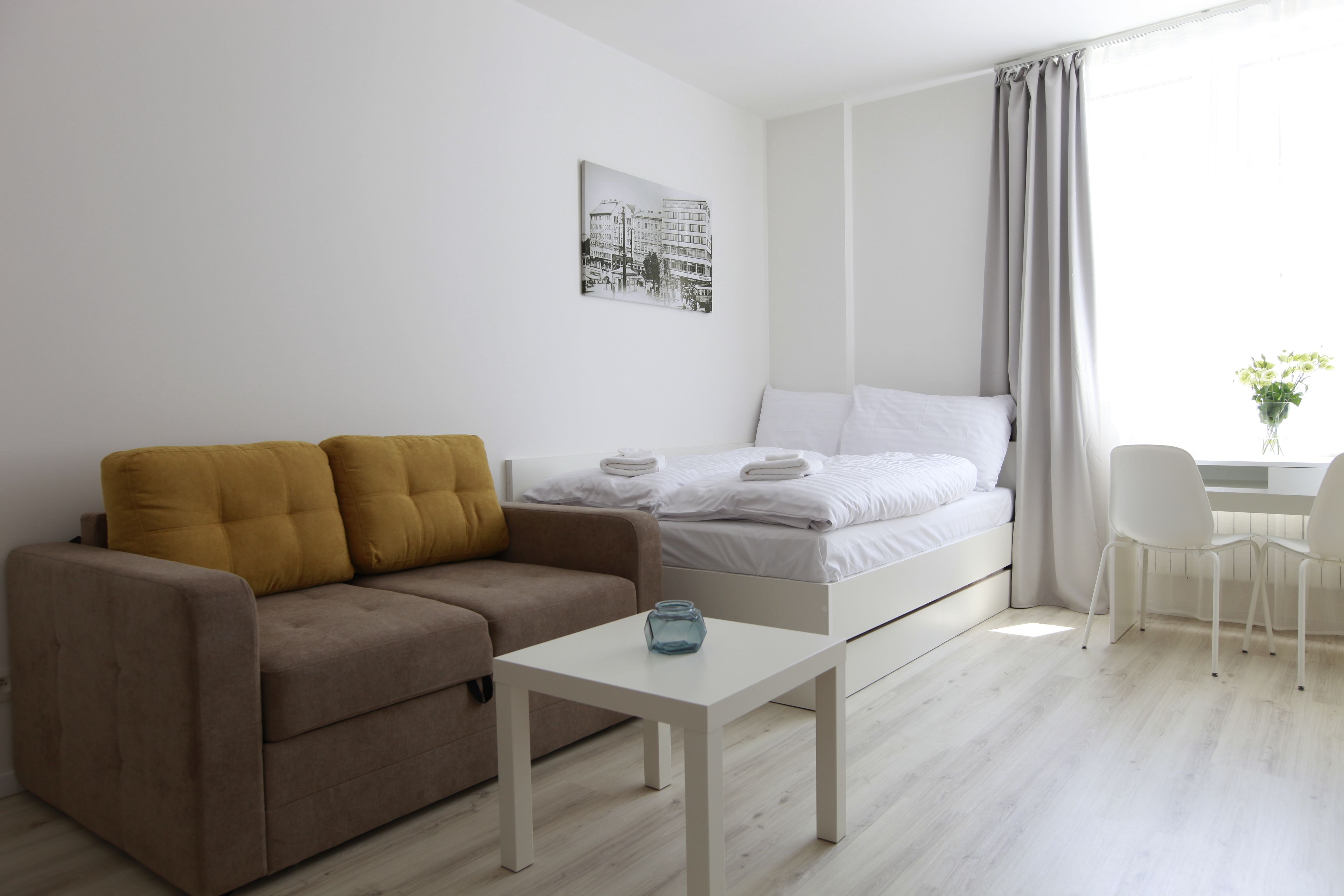 Une chambre à coucher moderne et minimaliste, avec un lit, un canapé, une petite table et une fenêtre avec des rideaux.
