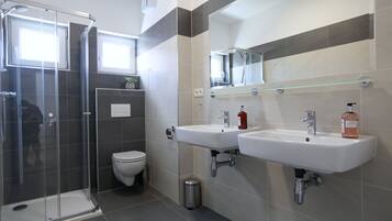 Een moderne badkamer met een douchecabine van glas, een toilet en twee wastafels met een spiegel erboven.