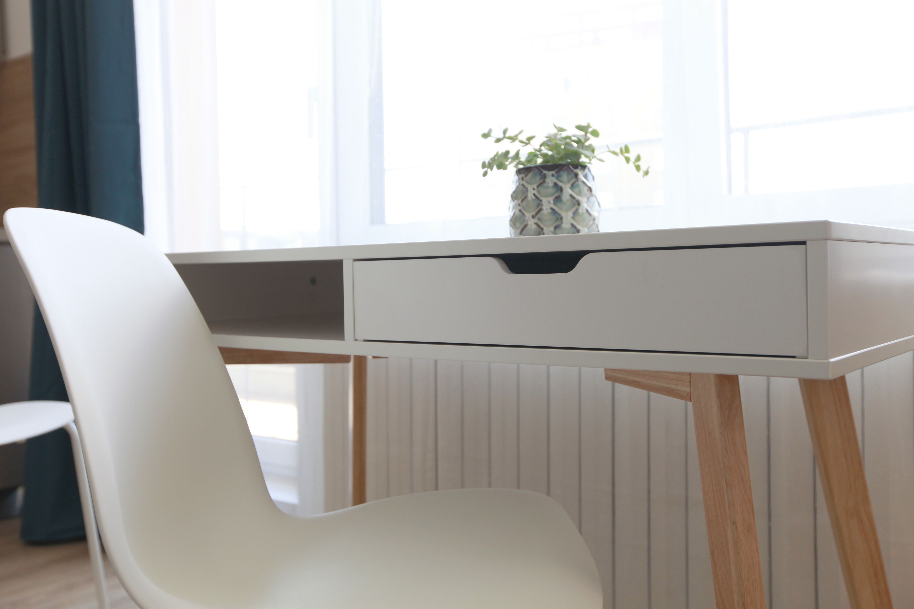 A white desk with a drawer, a white chair, and a potted plant on the desk.
