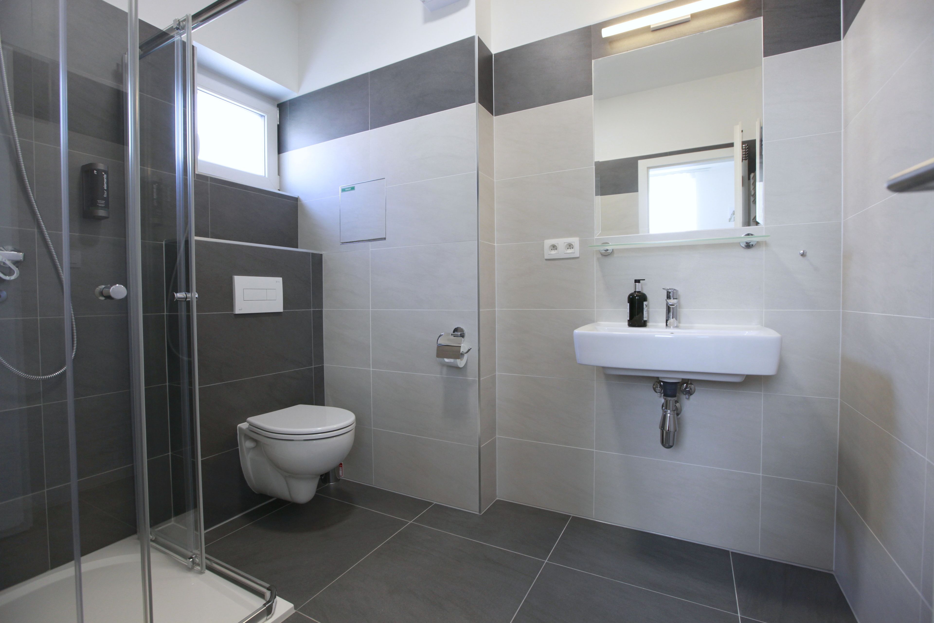 Un baño moderno con ducha envuelta en vidrio, inodoro y lavamanos con espejo superior.