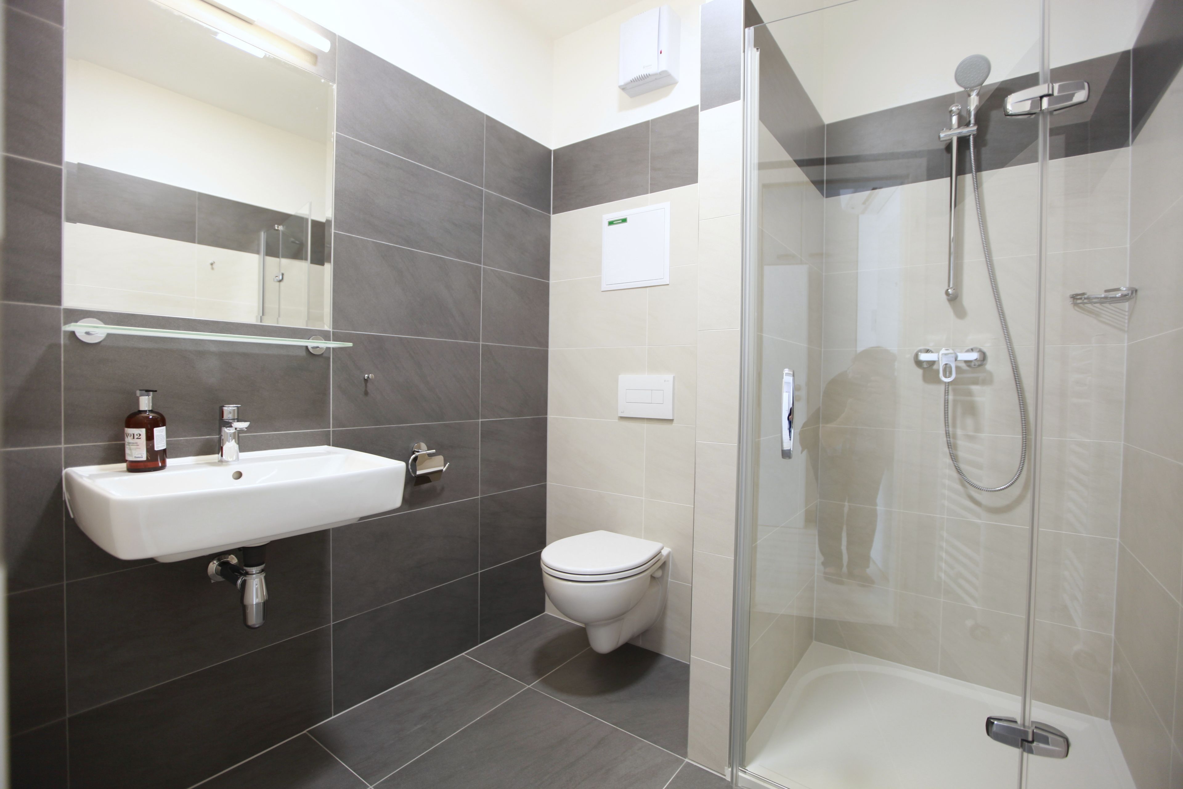 Un baño moderno con ducha envuelta en cristal, un lavamanos blanco y un inodoro.