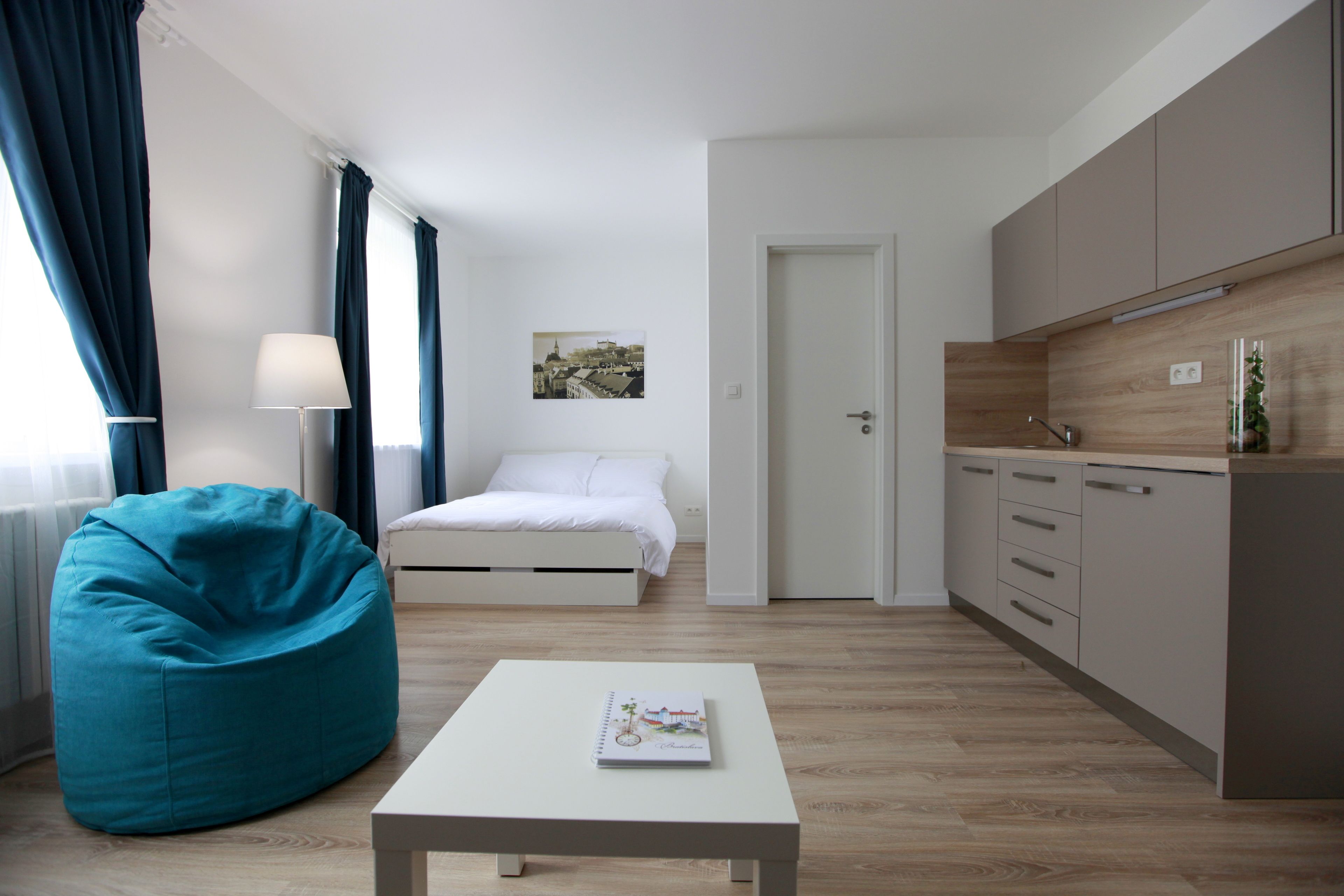 Ein modernes, minimalistisches Zimmer mit Bett, Sitzsack, kleinem Tisch und einer Küchenzeile.