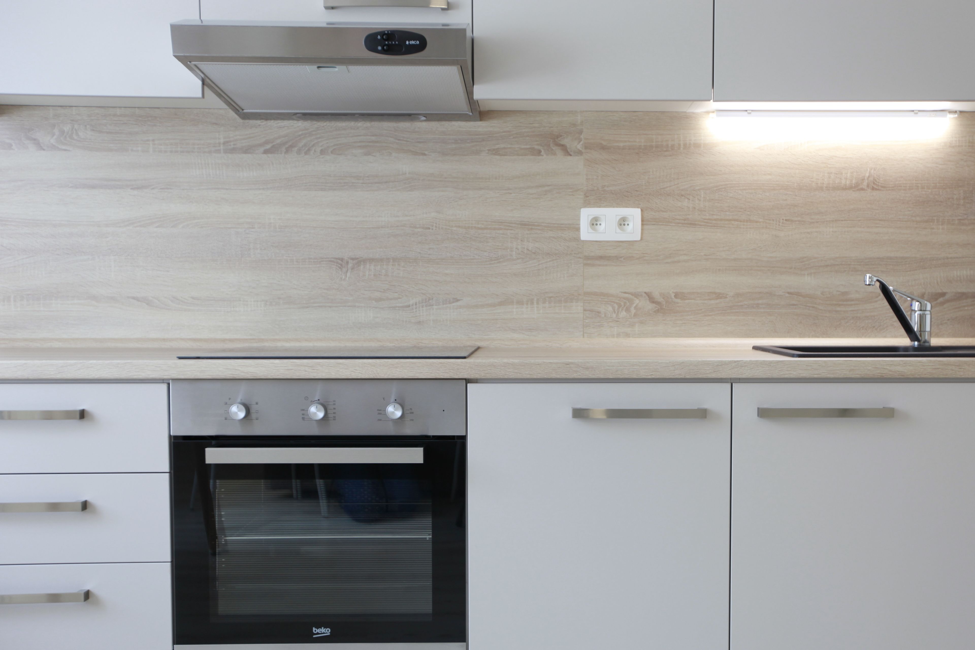 Una cocina moderna con horno empotrado, campana extractora de acero inoxidable y un salpicadero de madera claro.