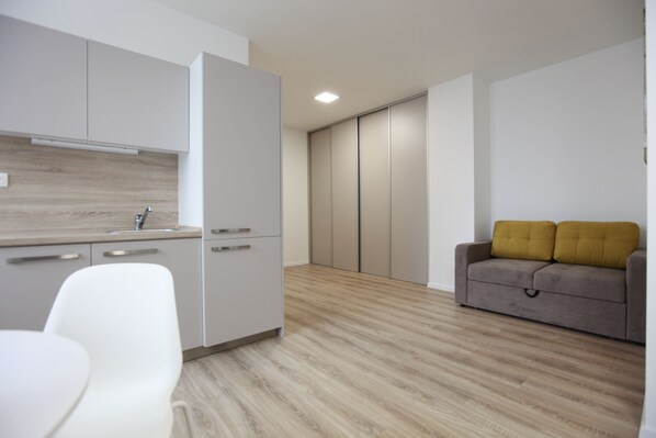 A modern kitchen with white cabinets, a wooden countertop, and a grey sofa with mustard cushions.