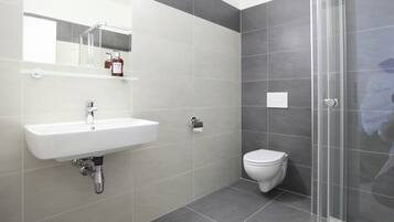 A modern bathroom with a white sink, a toilet, and a glass shower enclosure.