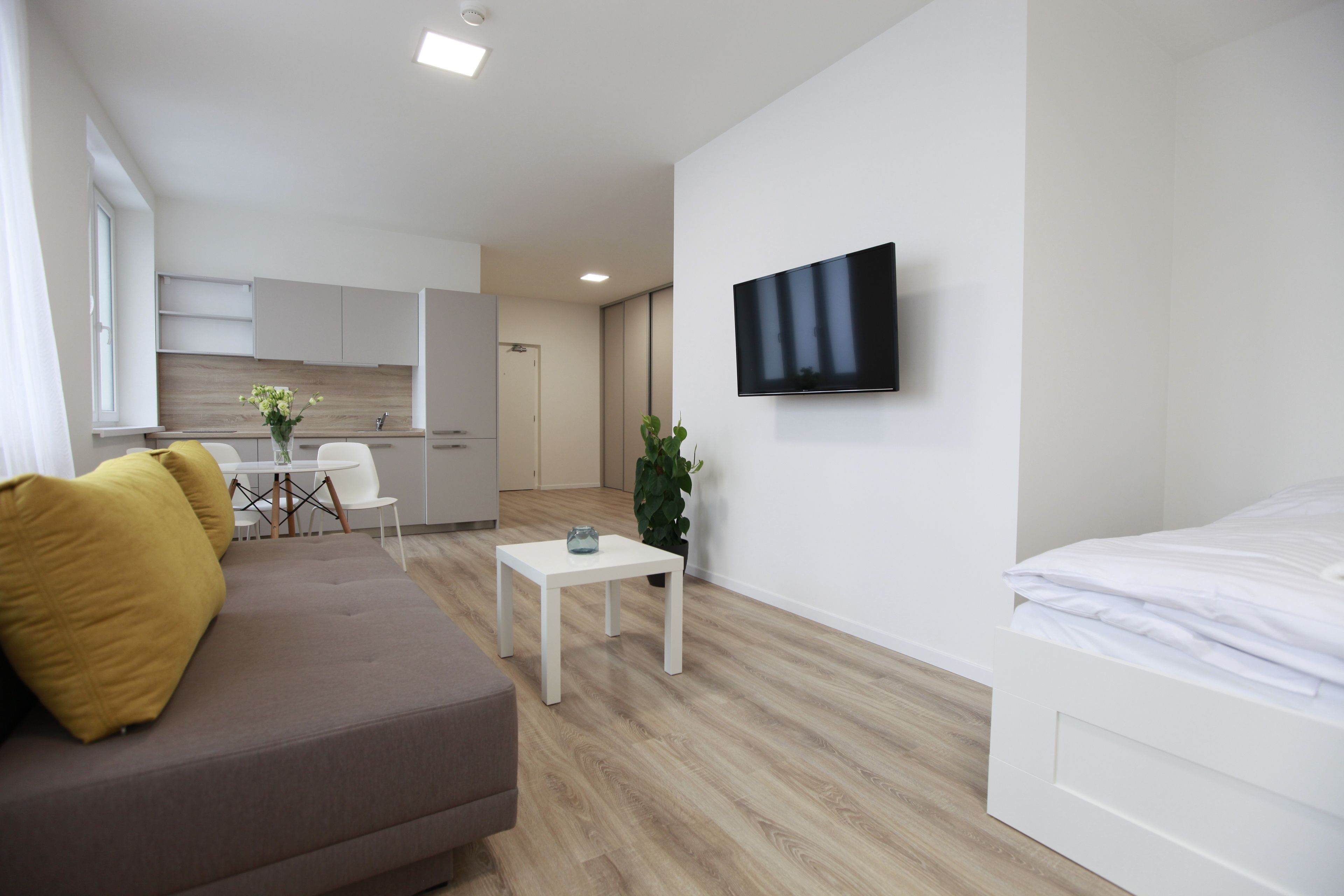 Una habitación moderna y bien iluminada con sofá, una mesita, televisor en la pared y cama.