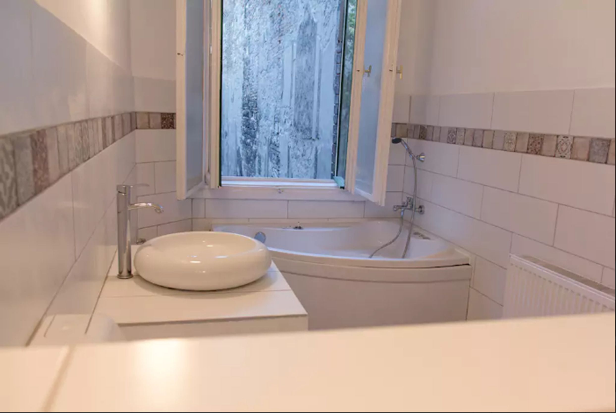 Un baño moderno con una bañera independiente, un lavabo redondo y una ventana con vistas a árboles.