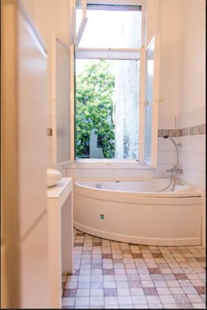 A bathroom with a bathtub, a window, and a tiled floor. - Incredible Ernesto IV (Budapest)