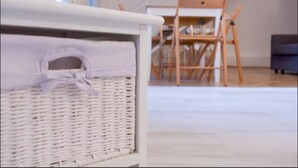 Un panier en osier avec une anse, posé sur un meuble blanc, une chaise en bois et un escalier en arrière-plan.