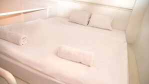 Un lit bien fait, avec du linge de lit blanc et des oreillers, une tête de lit blanche et une table de chevet blanche.